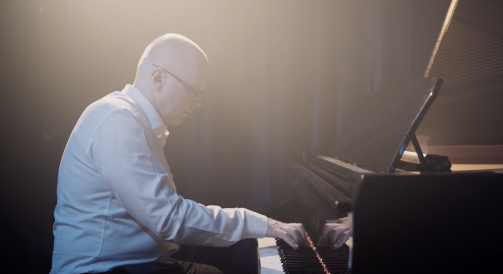 adult piano student wearing white shit playing a baby grand piano at a recitial 